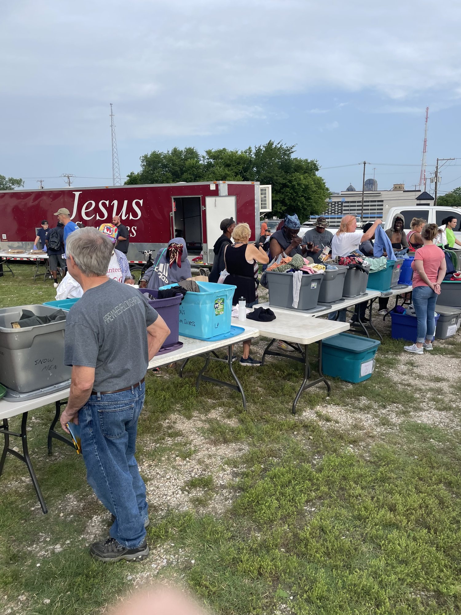 Tables of clothes and supplies beside the Jesus trailer at a homeless outreach